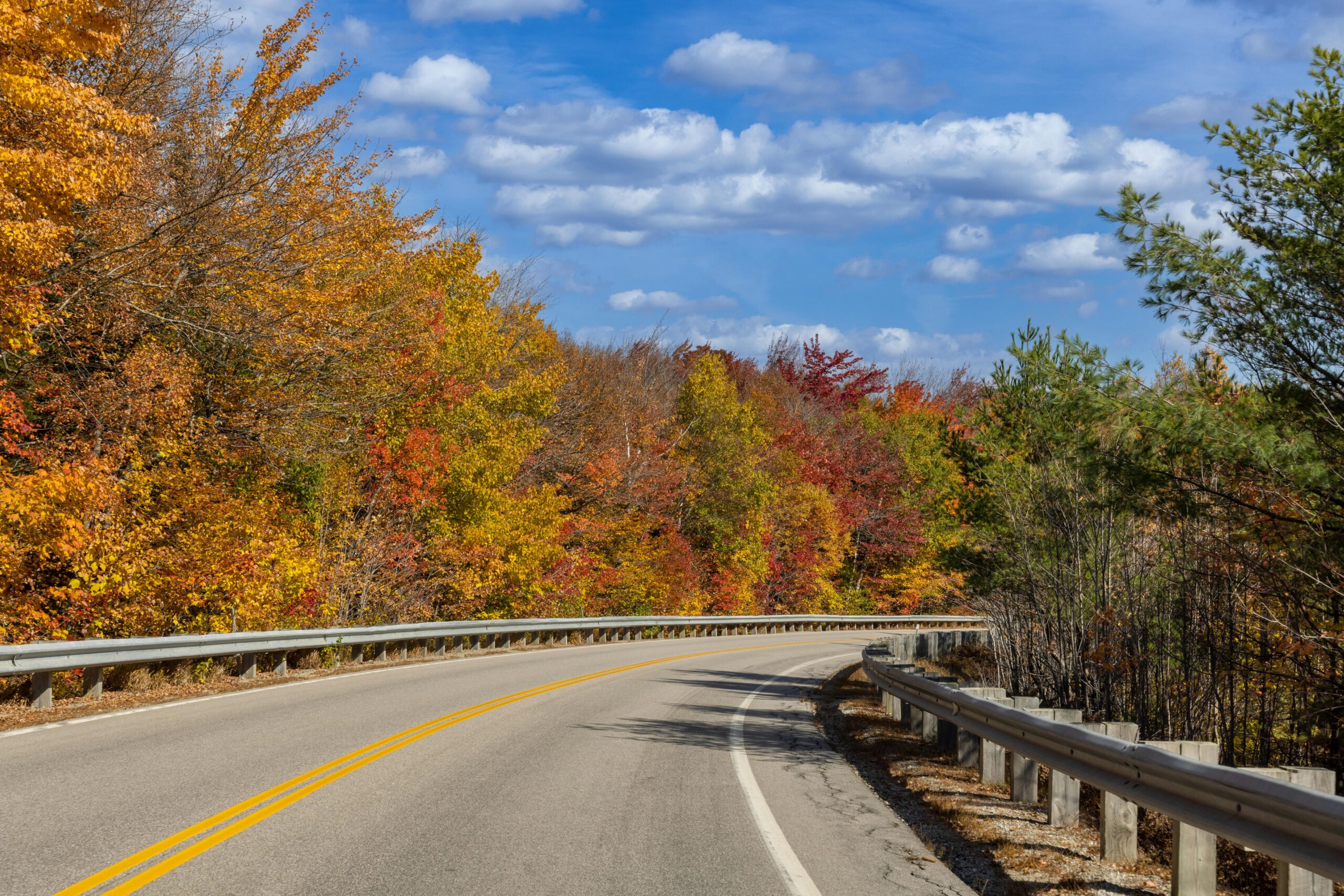 Home Vibrant fall foliage along a winding road in Franconia, NH, under a clear blue sky.